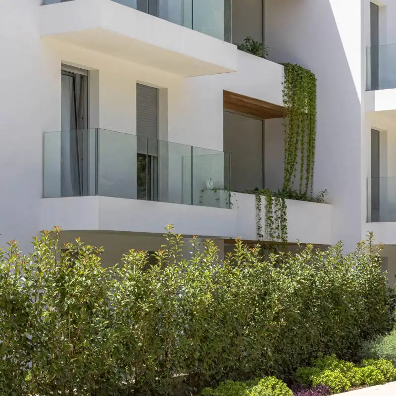 Edificio mediterráneo blanco con balcones de cristal y vegetación