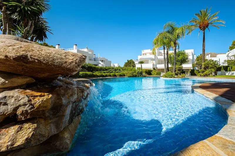 Piscina con cascada y palmeras en un complejo residencial mediterráneo